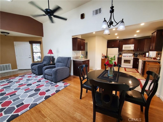 dining area featuring light hardwood / wood-style flooring, ceiling fan with notable chandelier, vaulted ceiling, and sink