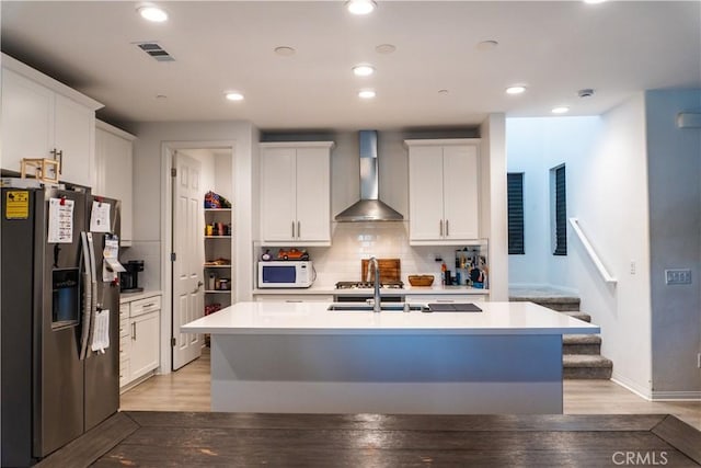 kitchen featuring stainless steel fridge with ice dispenser, a center island with sink, white cabinetry, and wall chimney exhaust hood