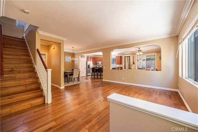 unfurnished living room with ceiling fan with notable chandelier, crown molding, and wood-type flooring