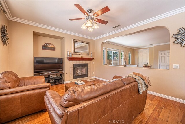 living room with a fireplace, light hardwood / wood-style floors, crown molding, and ceiling fan