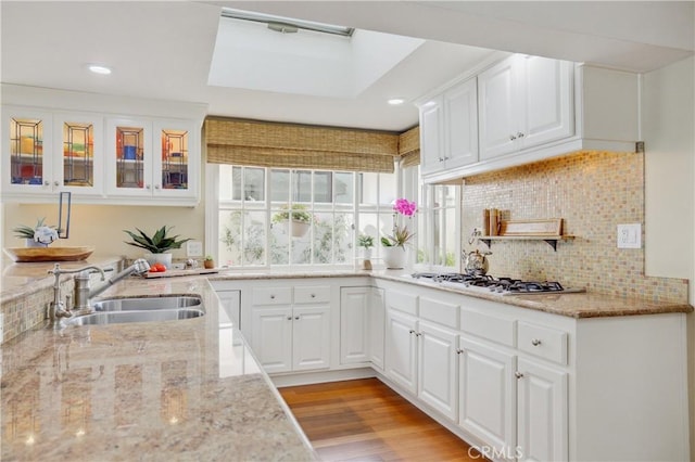 kitchen featuring stainless steel gas stovetop, light stone countertops, white cabinets, and sink