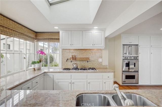 kitchen with a skylight, sink, white cabinetry, and stainless steel appliances