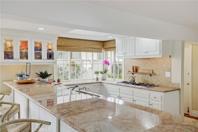 kitchen with tasteful backsplash, stainless steel gas stovetop, white cabinetry, a breakfast bar area, and light stone counters