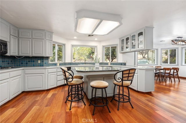 kitchen featuring light wood-type flooring, decorative backsplash, a kitchen island, and a kitchen breakfast bar