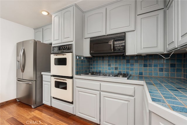 kitchen with light wood-type flooring, tile counters, decorative backsplash, and stainless steel appliances