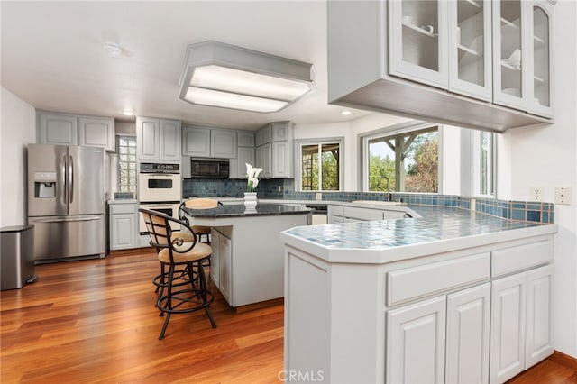 kitchen with a kitchen breakfast bar, stainless steel fridge, light hardwood / wood-style floors, a kitchen island, and double oven