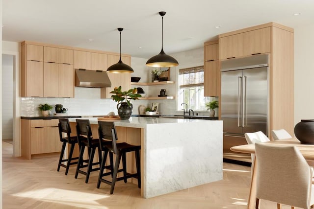 kitchen featuring built in fridge, ventilation hood, light parquet floors, light brown cabinetry, and a kitchen island