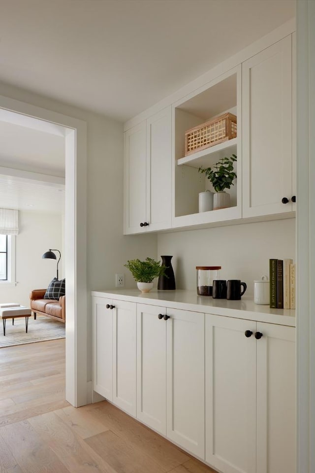 bar with white cabinets and light hardwood / wood-style flooring