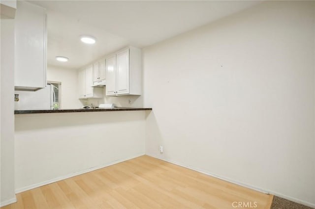 kitchen with white cabinetry, white refrigerator, kitchen peninsula, and light wood-type flooring