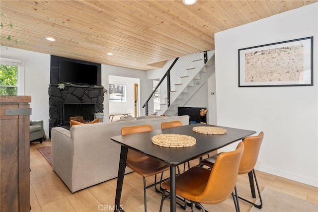 dining area with a stone fireplace, light wood-type flooring, and wood ceiling