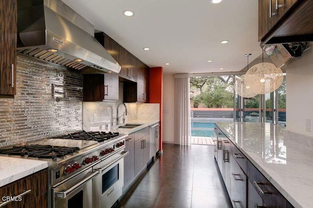 kitchen with light stone countertops, sink, stainless steel appliances, wall chimney range hood, and tasteful backsplash