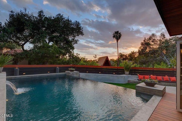 pool at dusk with pool water feature and a wooden deck