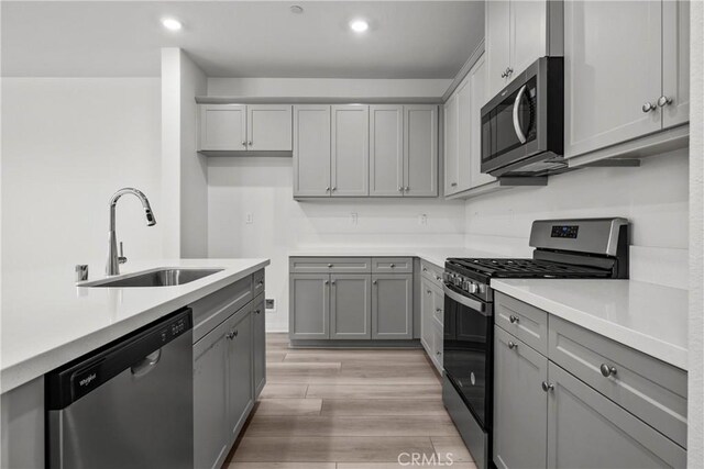 kitchen with gray cabinets, sink, appliances with stainless steel finishes, and light hardwood / wood-style flooring