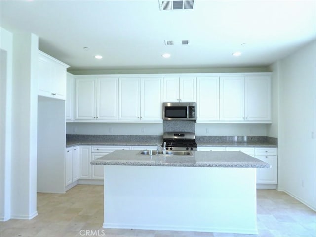 kitchen featuring white cabinets, stainless steel appliances, light stone counters, and a center island with sink