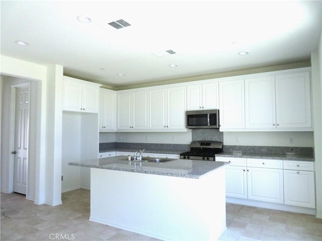 kitchen with white cabinetry, sink, stainless steel appliances, dark stone counters, and a kitchen island with sink