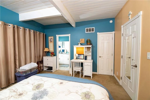 bedroom with beam ceiling, ensuite bath, and light colored carpet