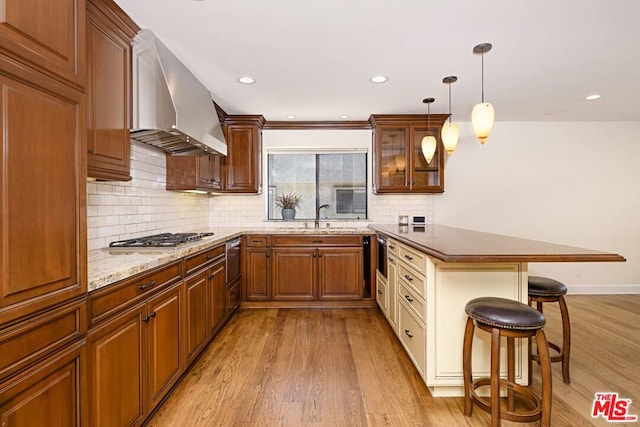 kitchen featuring pendant lighting, sink, wall chimney exhaust hood, light hardwood / wood-style floors, and a breakfast bar area