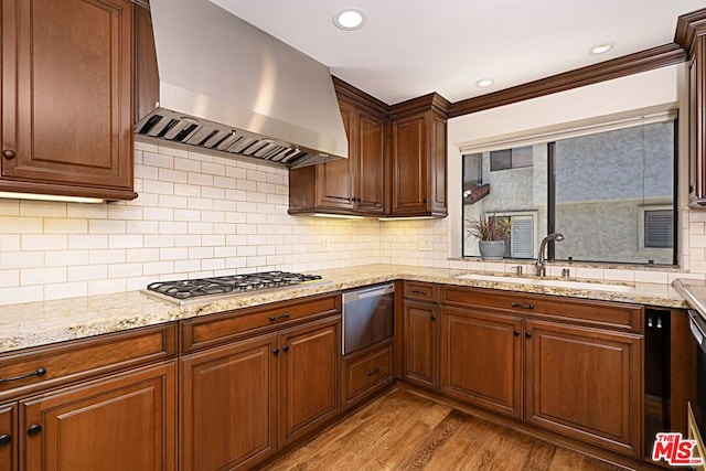 kitchen with sink, wall chimney exhaust hood, light wood-type flooring, tasteful backsplash, and stainless steel gas cooktop