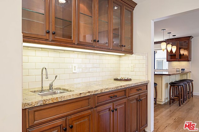 kitchen featuring light stone countertops, backsplash, sink, light hardwood / wood-style flooring, and hanging light fixtures