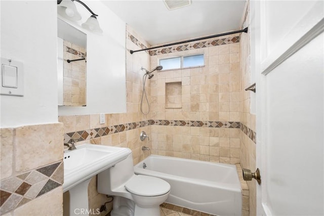 bathroom with tiled shower / bath, toilet, and tile walls