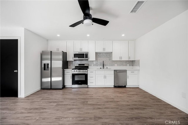 kitchen featuring sink, backsplash, hardwood / wood-style floors, white cabinets, and appliances with stainless steel finishes