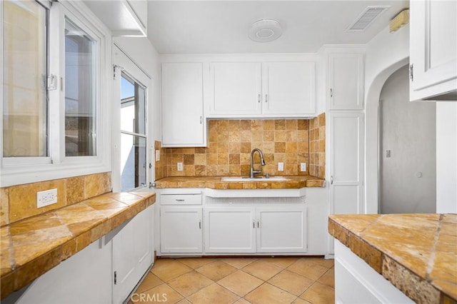 kitchen featuring tile countertops, backsplash, sink, light tile patterned flooring, and white cabinetry