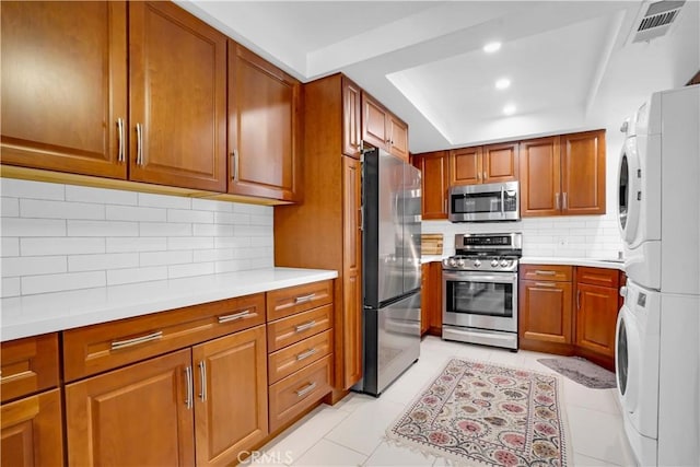 kitchen with stacked washing maching and dryer, backsplash, stainless steel appliances, and light tile patterned flooring