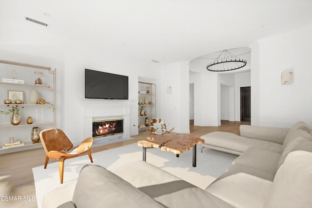 living room featuring light hardwood / wood-style flooring, a notable chandelier, and built in features