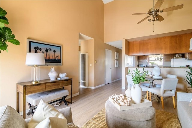 living room featuring ceiling fan, a high ceiling, and light hardwood / wood-style flooring