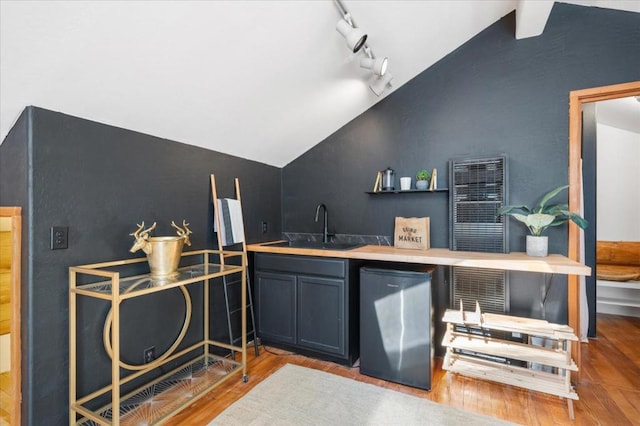 bar with light wood-type flooring, vaulted ceiling, stainless steel refrigerator, and sink