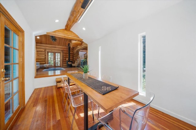 dining space featuring wood-type flooring, vaulted ceiling with beams, and a wood stove