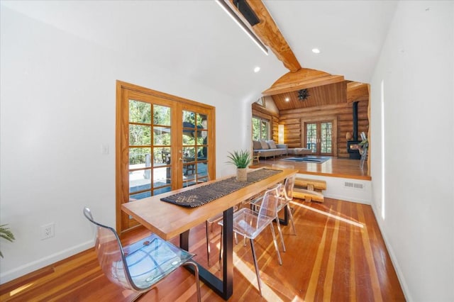 dining area with a wood stove, lofted ceiling with beams, hardwood / wood-style flooring, and french doors