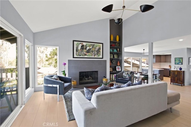 living room featuring built in features, vaulted ceiling, a wealth of natural light, and a tiled fireplace