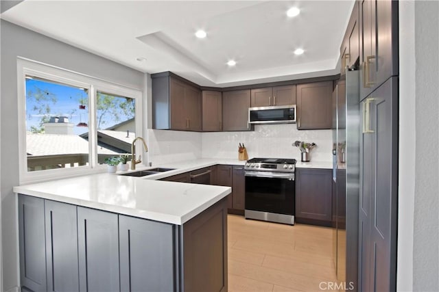 kitchen featuring dark brown cabinetry, stainless steel appliances, sink, kitchen peninsula, and a tray ceiling