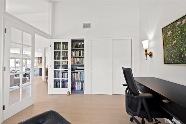 office featuring a towering ceiling, french doors, and light hardwood / wood-style flooring