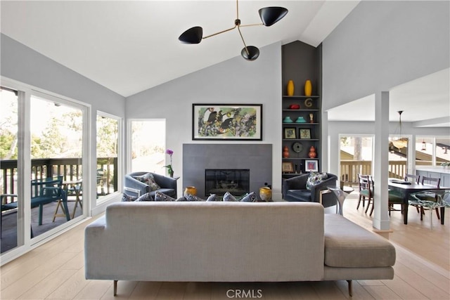 living room with built in shelves, light hardwood / wood-style floors, and vaulted ceiling