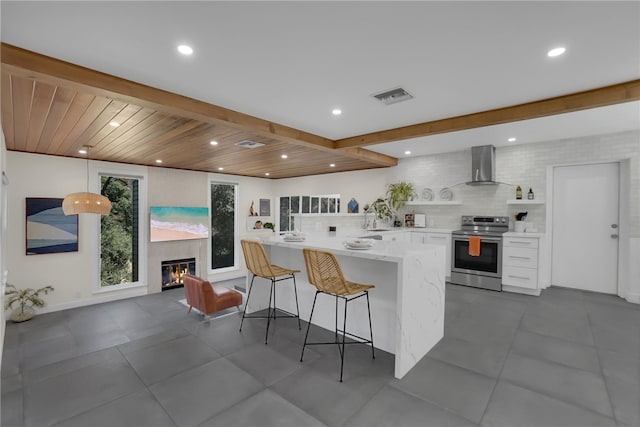 kitchen with a kitchen bar, wood ceiling, stainless steel electric range oven, wall chimney range hood, and white cabinetry