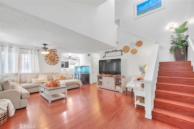 living room featuring ceiling fan, hardwood / wood-style flooring, a textured ceiling, and a high ceiling