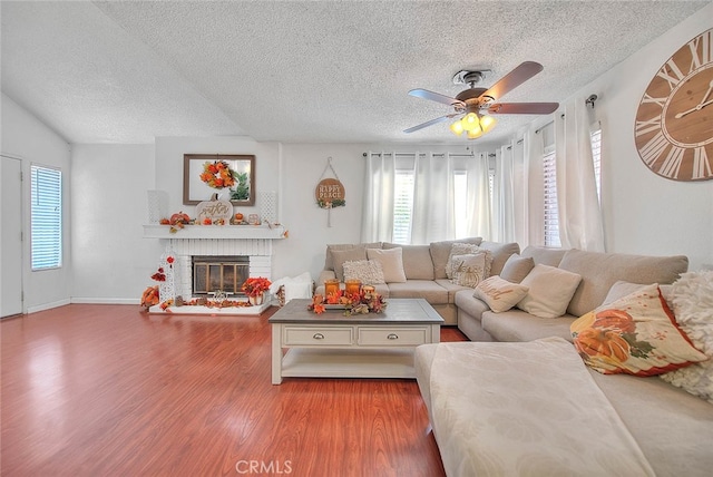 living room featuring a textured ceiling, a fireplace, wood-type flooring, and ceiling fan