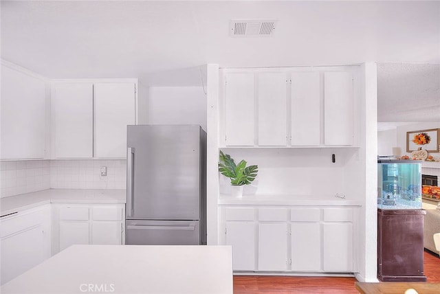 kitchen with white cabinetry, light hardwood / wood-style floors, backsplash, and stainless steel fridge