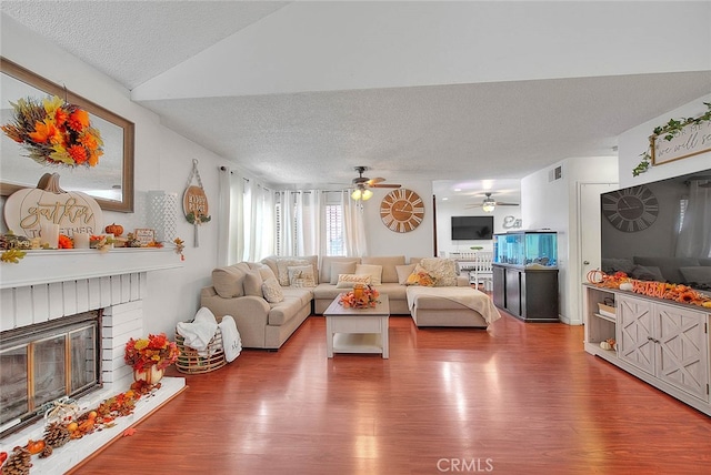 living room with ceiling fan, hardwood / wood-style flooring, a textured ceiling, and a brick fireplace