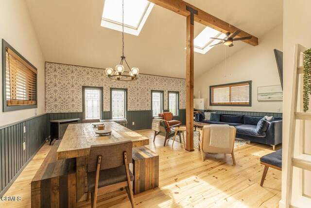 dining area with high vaulted ceiling, ceiling fan with notable chandelier, a skylight, light wood-type flooring, and beamed ceiling