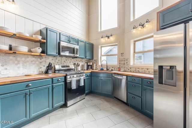 kitchen featuring wooden counters, stainless steel appliances, blue cabinets, sink, and a high ceiling