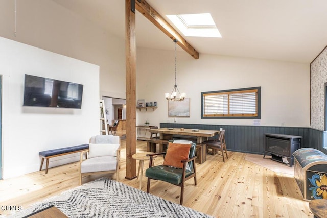 living room with a notable chandelier, light hardwood / wood-style floors, a wood stove, and lofted ceiling with skylight