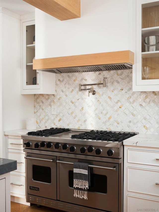 kitchen with backsplash, white cabinets, range with two ovens, and light stone countertops