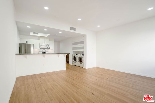 kitchen featuring white cabinets, washer and dryer, stainless steel fridge, light wood-type flooring, and kitchen peninsula