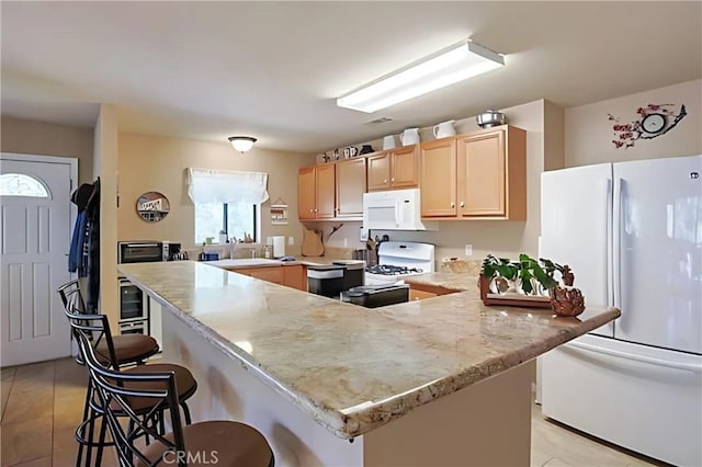 kitchen featuring light brown cabinets, sink, kitchen peninsula, white appliances, and a kitchen breakfast bar