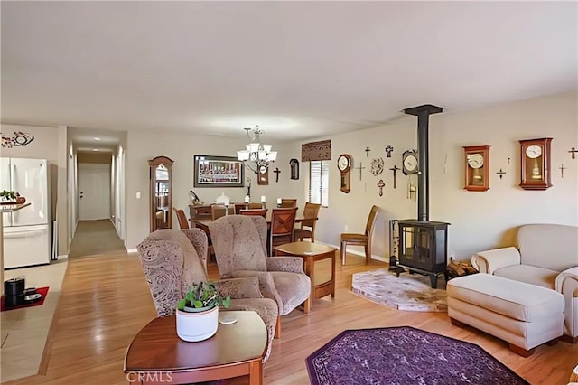 living room featuring light hardwood / wood-style flooring, a wood stove, and a notable chandelier