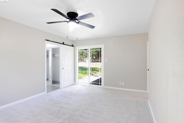 unfurnished bedroom featuring access to exterior, light colored carpet, ceiling fan, a barn door, and a closet