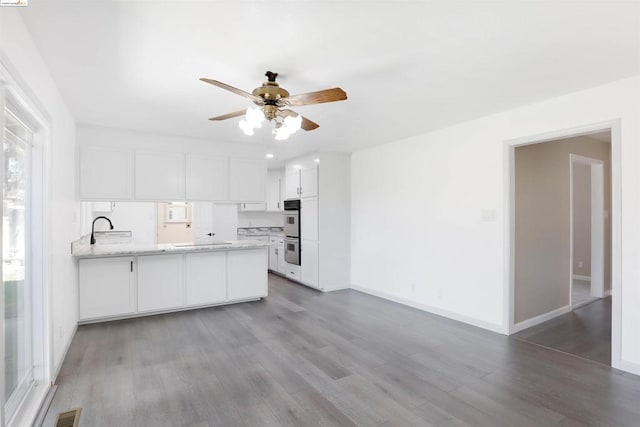 kitchen with sink, double oven, kitchen peninsula, white cabinets, and hardwood / wood-style flooring